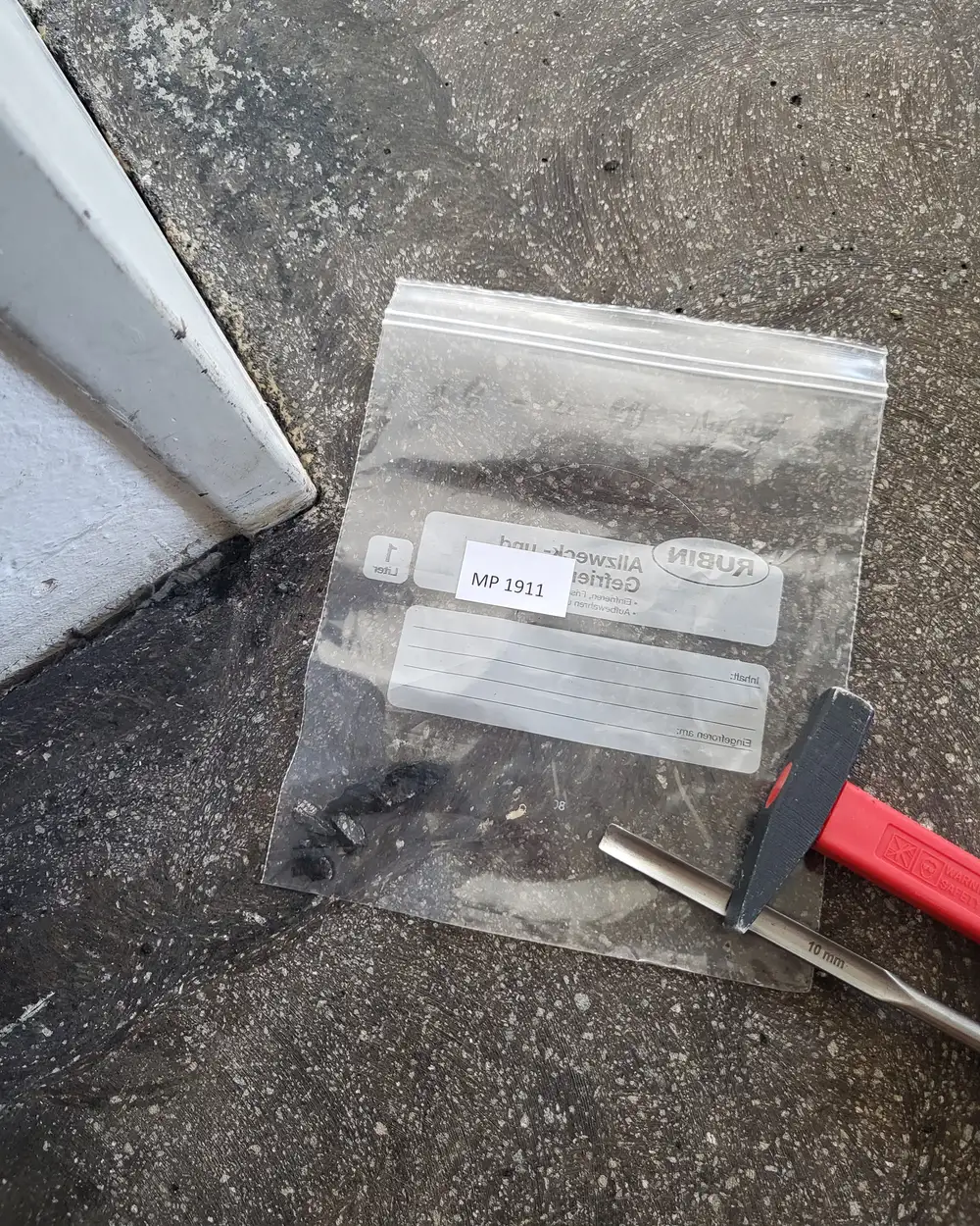 Materialprobe in einem beschrifteten Probenbeutel, daneben Hammer und Meißel