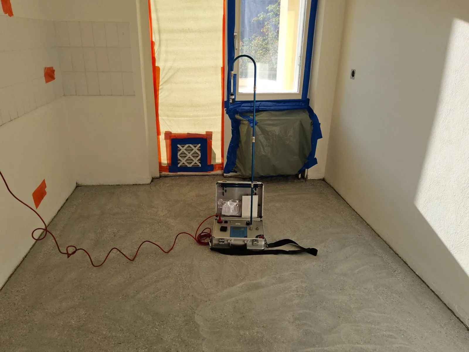 Raumluftmessung in einem sanierten Raum: Messgerät mit Ansaugrohr, Fenster und Heizkörper mit Folie abgeklebt